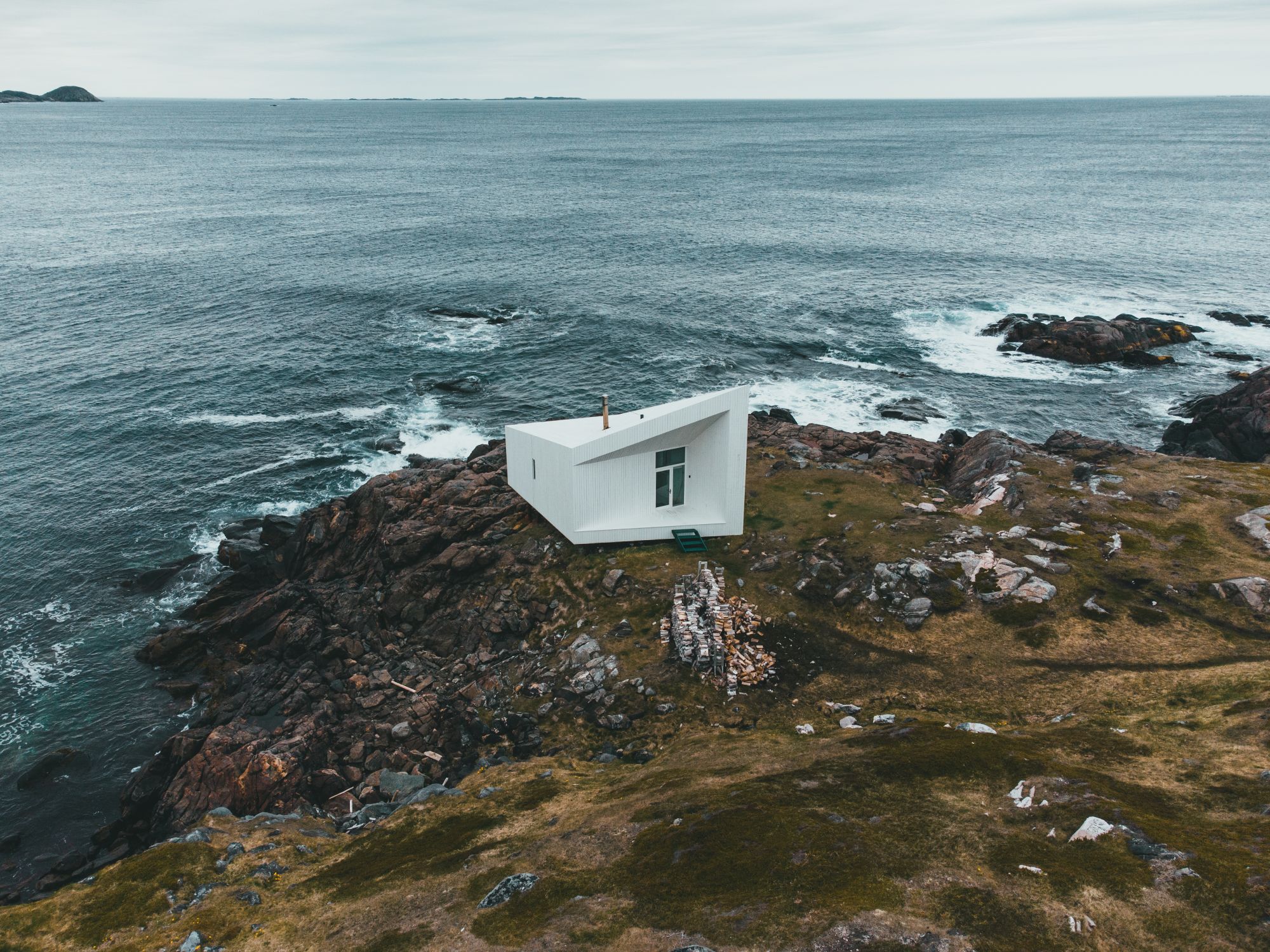 Aerial view of a white contemporary cabin on a rocky headland above the Atlantic