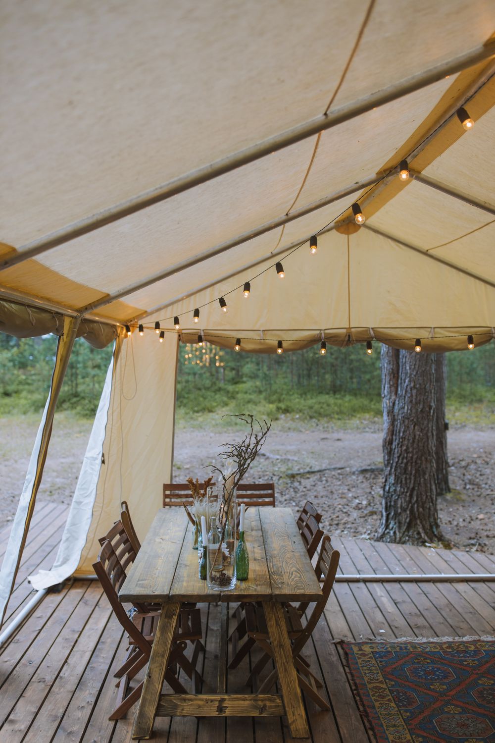 Outdoor dining table under a canvas canopy strung with festoon lights