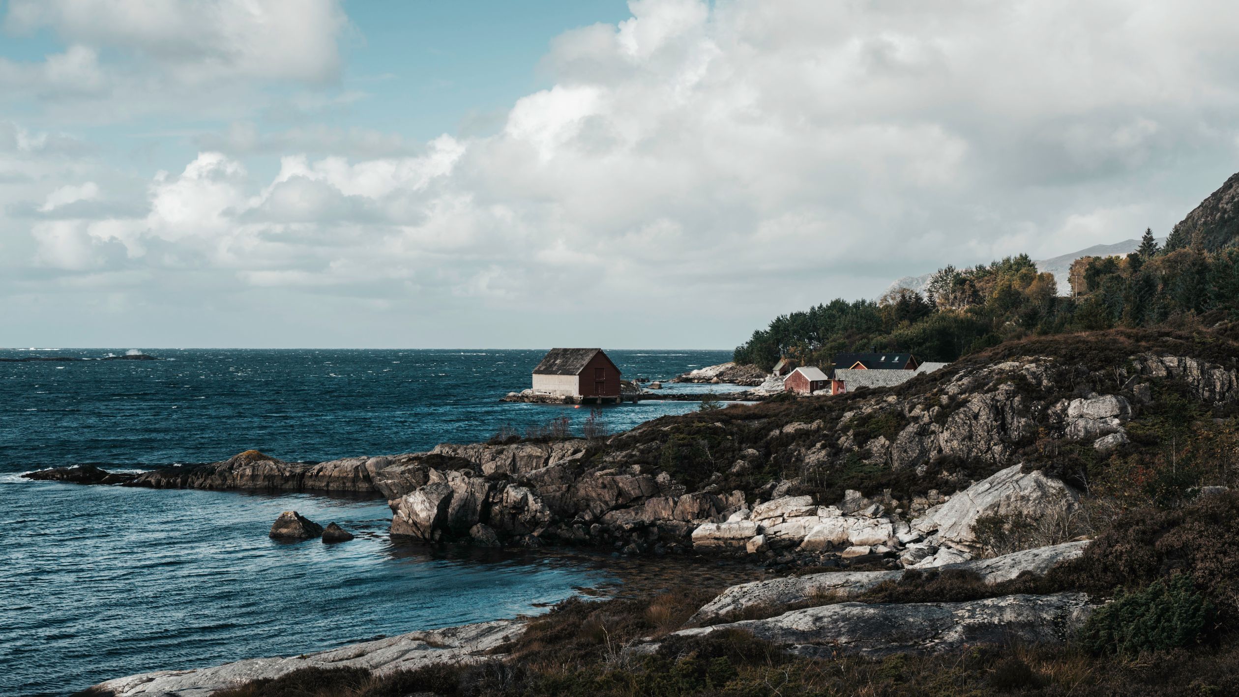 Red boathouses on a rocky shore with waves rolling in