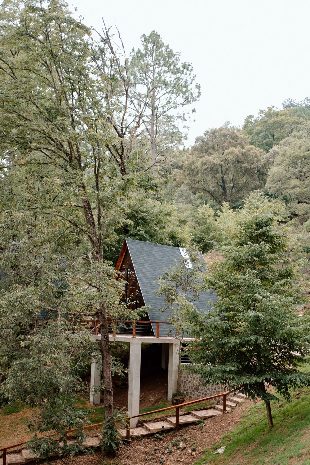 A-frame cabin raised on a concrete base among broadleaf trees